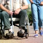 Persona con disabilità in una situazione di assistenza, simbolo di invalidità civile al 100% e indennità di accompagnamento.